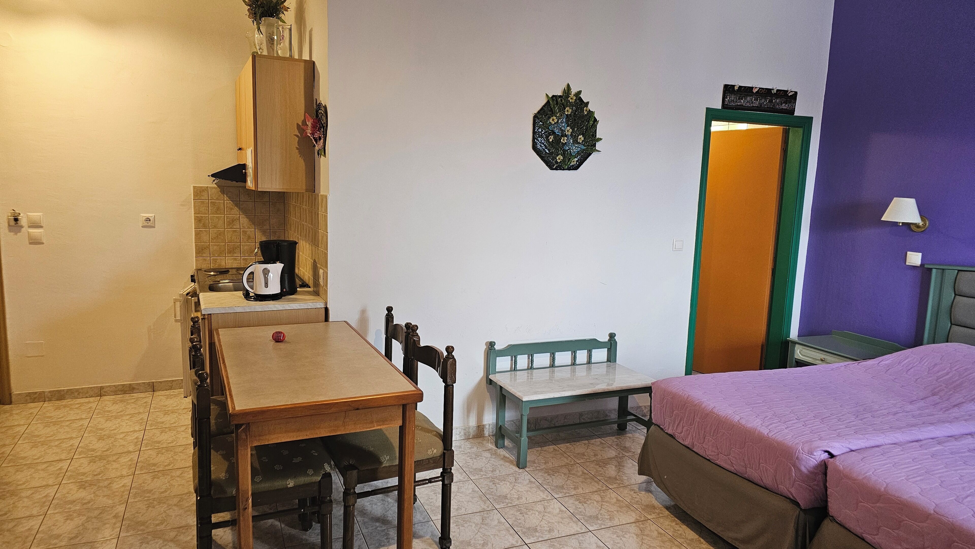 A small, compact room with a kitchenette, a bed, a small table, and a bench.