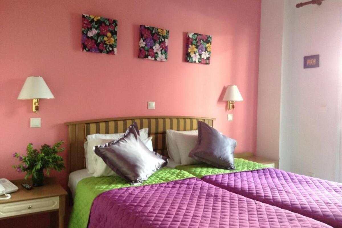 A room with a bed, two bedside lamps, a nightstand with a phone, and floral artwork on the wall.
