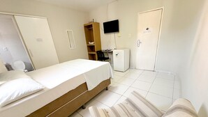 A hotel room with a bed, a small desk, a television, a wardrobe, and a door. - HOTEL OITICICA (Fortaleza)