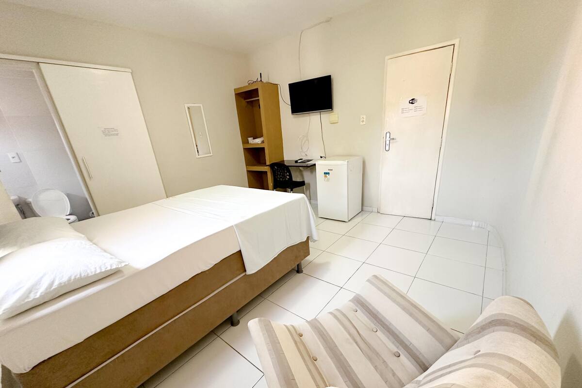 A hotel room with a bed, a small desk, a television, a wardrobe, and a door.