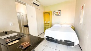 A hotel room with a bed, a desk with a telephone and keys, a bathroom with a sink, and an air conditioning unit. - HOTEL OITICICA (Fortaleza)
