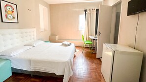 A bedroom with a bed, a desk, a chair, a television, and a refrigerator. - HOTEL OITICICA (Fortaleza)