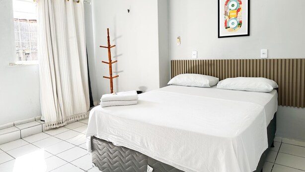 A modern bedroom with a bed, a window with curtains, a wall-mounted light, and a framed picture. - HOTEL OITICICA (Fortaleza)