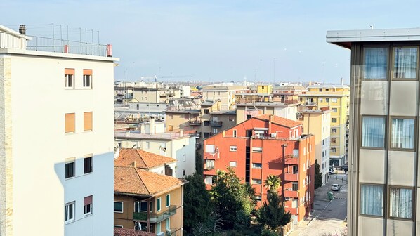 Un edificio residencial de varios pisos con balcones, fachada roja y vista de un paisaje urbano con diversos edificios.