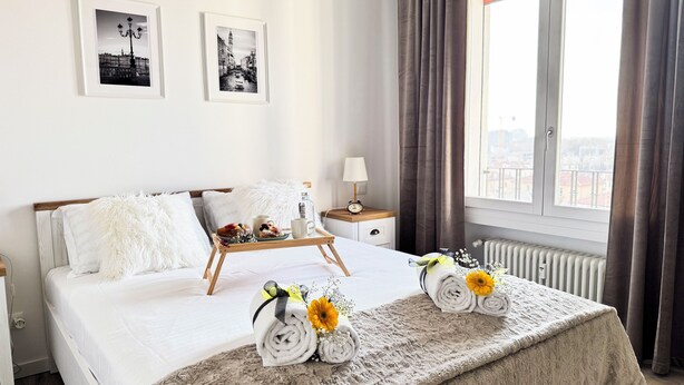 A hotel room with a bed, a nightstand, a window with curtains, and two framed pictures on the wall.