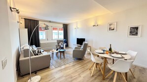 A modern living room with a sofa, TV, and dining area with chairs and a table.