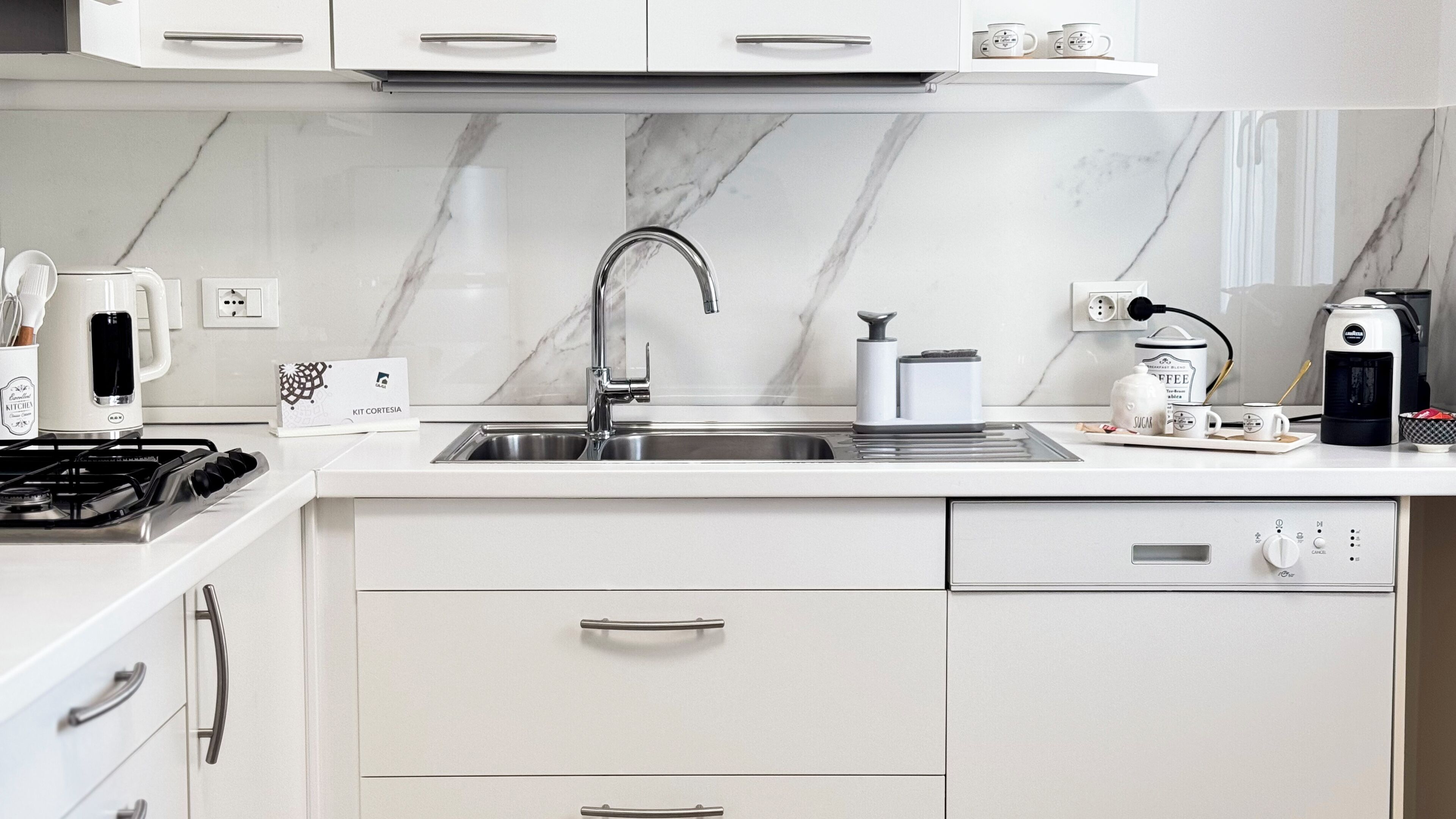 Une cuisine moderne dotée d’un évier en acier inoxydable, de meubles blancs et d’une cuisinière à gaz.