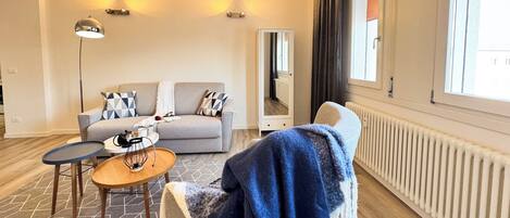 A modern living room with a sofa, a small table, a floor lamp, a mirror, and a radiator.