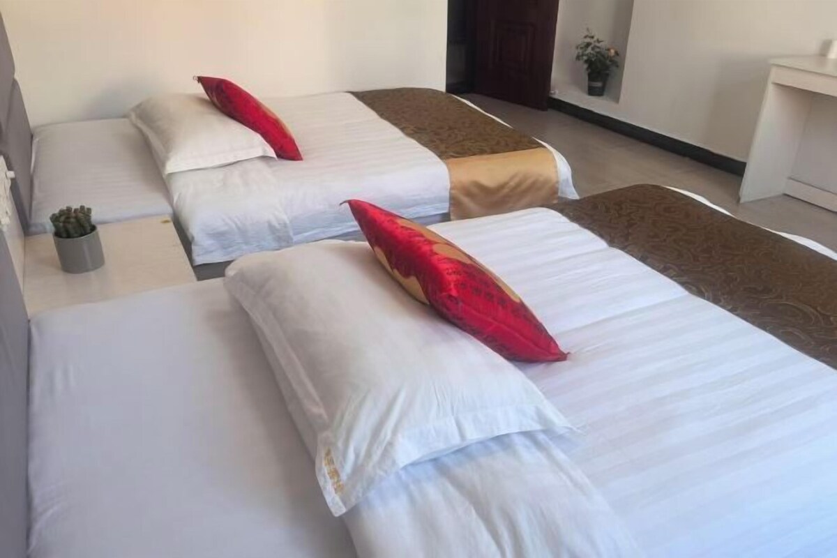 Three single beds with white and red pillows, a small potted plant, and a brown decorative runner.