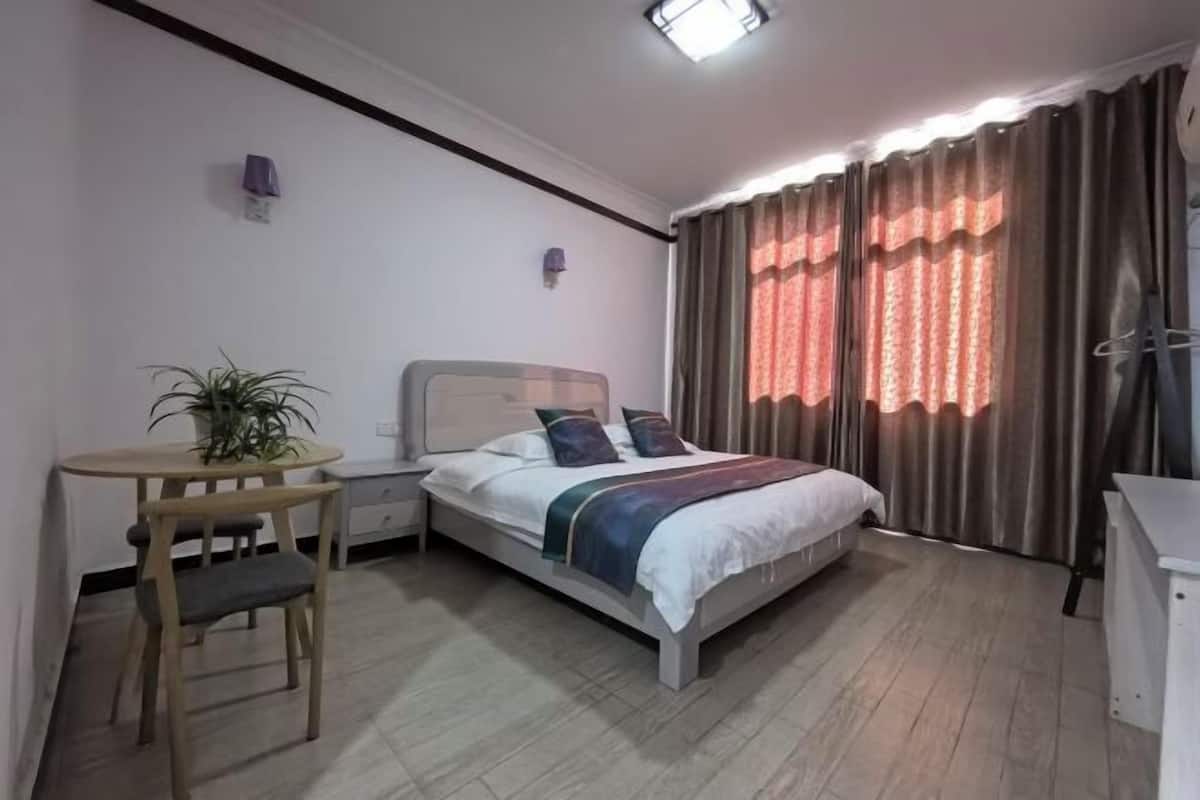 A bedroom with a bed, bedside tables, a small table with a chair, and a potted plant.
