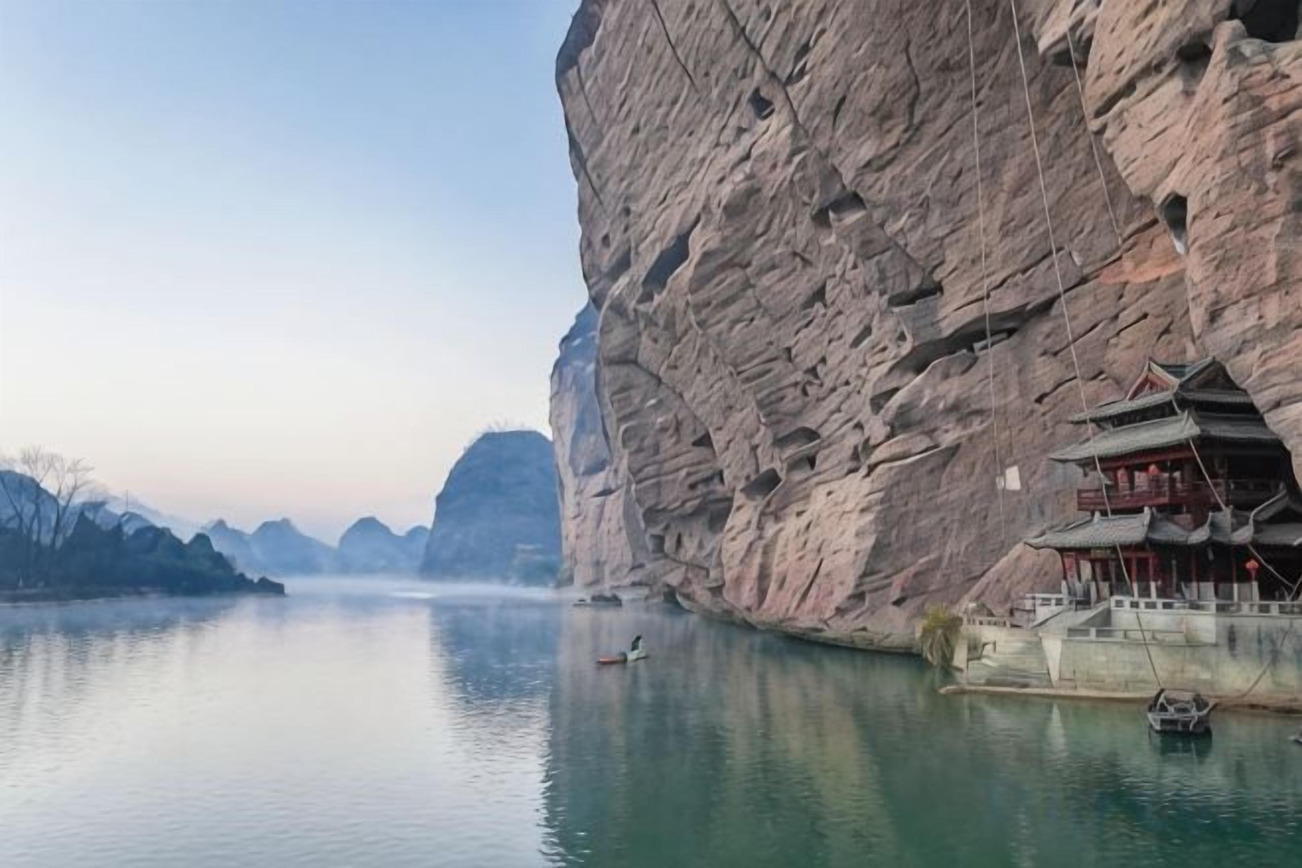 A traditional building with a steep cliffside, a calm river, and a small boat.