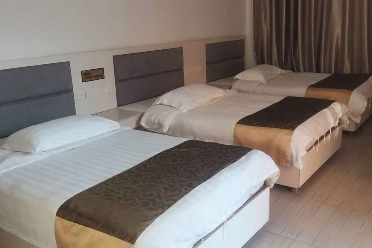 A hotel room with three beds, each with a headboard and a bedside table.