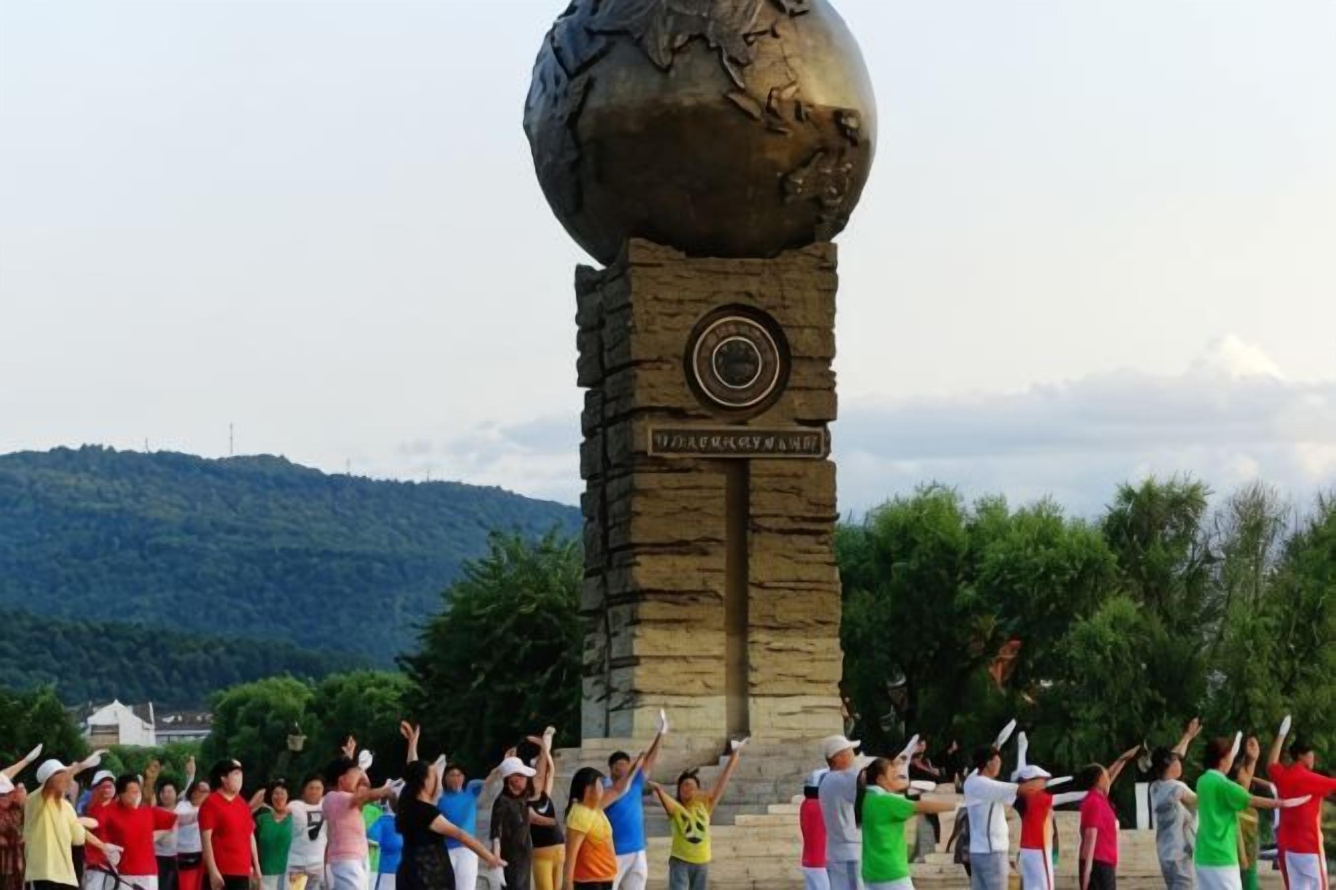 Eine Gruppe von Menschen führt Übungen vor einem Denkmal mit einem Globus auf der Spitze vor einer bergigen Landschaft aus.