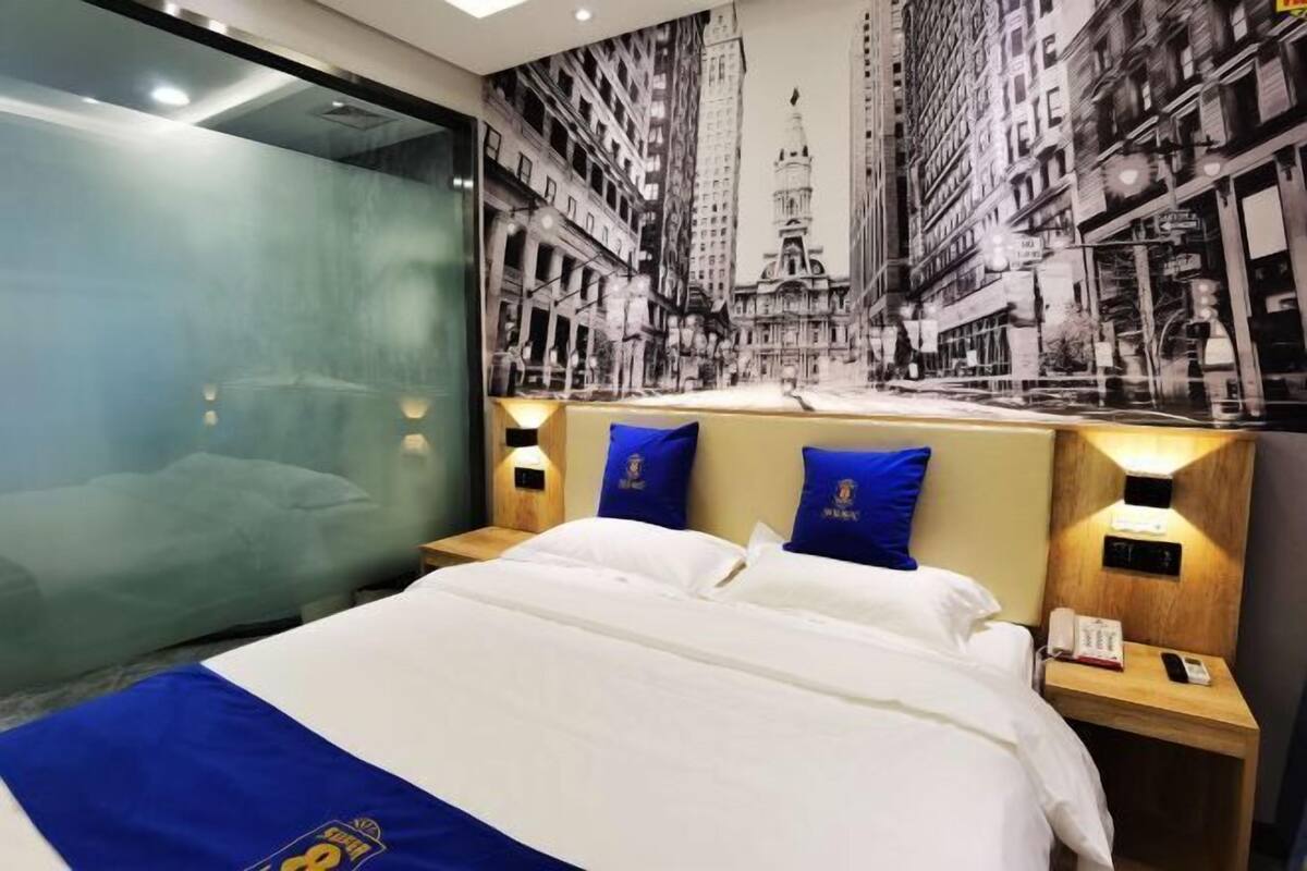 A hotel room with a large bed, a glass wall, and a cityscape mural on the wall.
