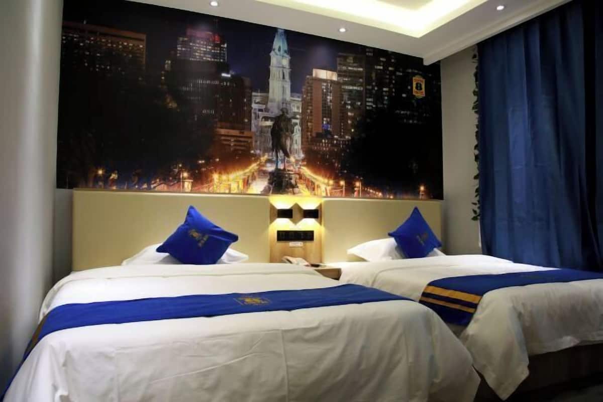 A hotel room with two beds, a cityscape mural, and a night-time city view.