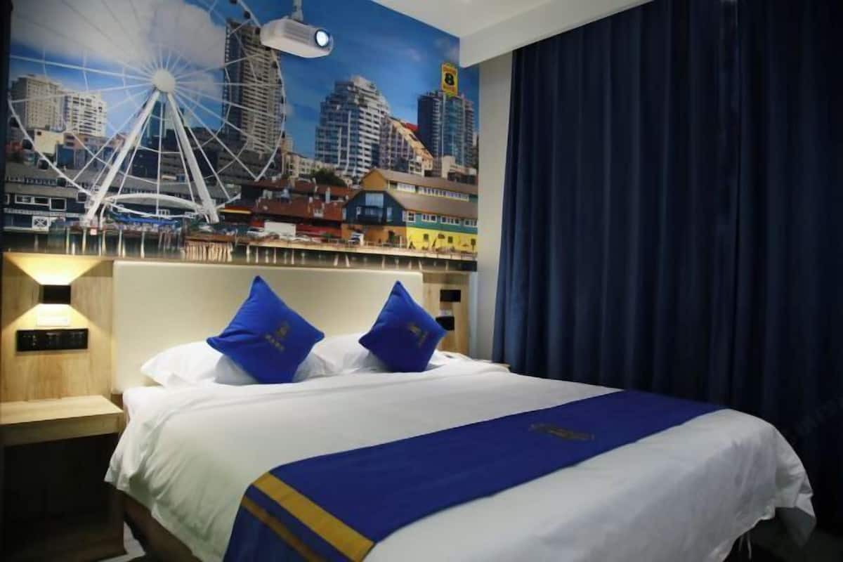 A hotel room with a bed, a cityscape mural, a projector, and a nightstand.
