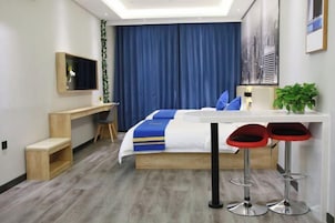 Habitación de hotel moderna con cama, escritorio, silla, televisor y dos taburetes de bar.