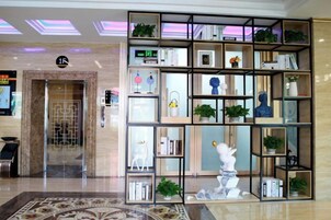 Un hall con mostrador de recepción, zona de espera y una estantería decorativa con varios objetos.