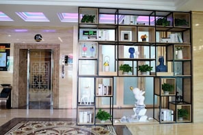 Un hall con mostrador de recepción, zona de espera y una estantería decorativa con varios objetos.