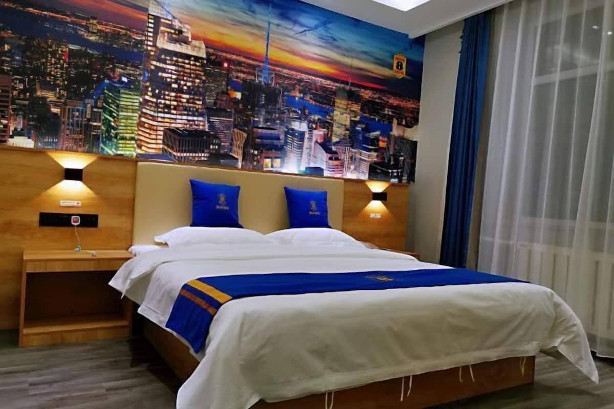A hotel room with a bed, two nightstands, a cityscape mural on the wall, and a window with curtains.