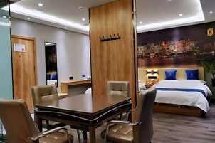 A hotel room with a cityscape view, a bed with blue pillows, a desk with a chair, and a wooden partition.