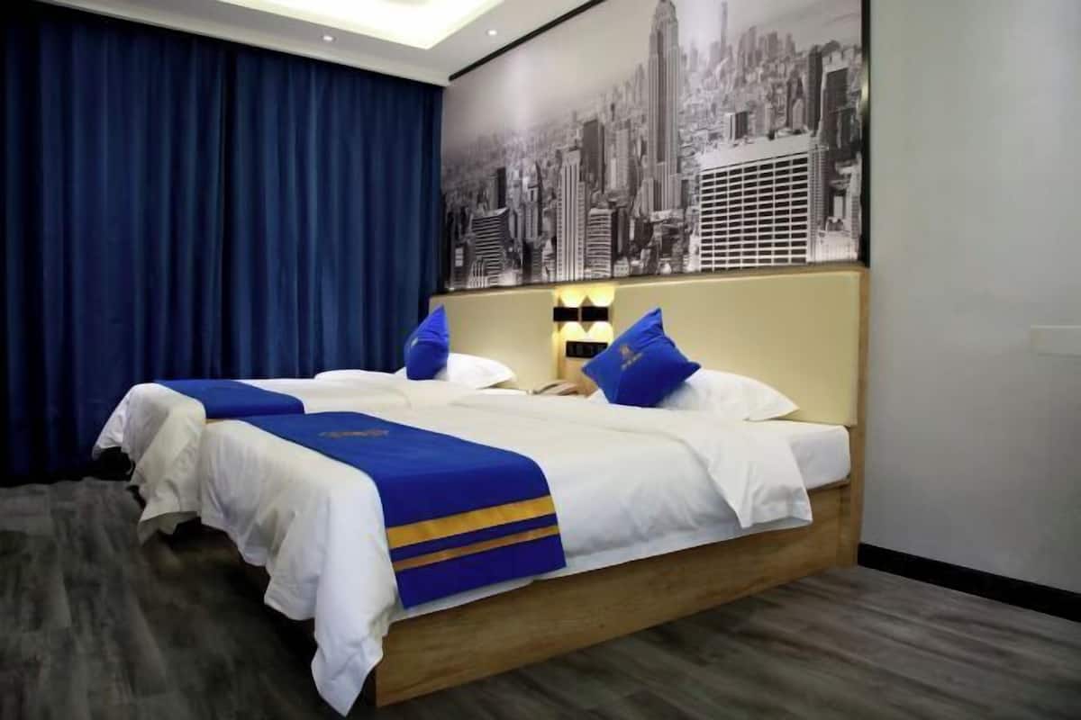A hotel room with a large bed, blue and white bedding, a cityscape mural, and a dark blue curtain.