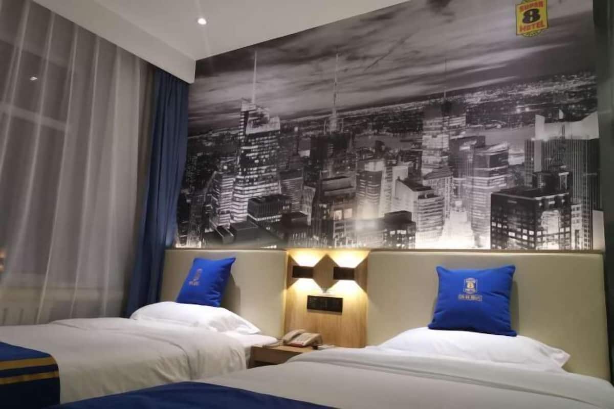 A hotel room with two beds, a cityscape mural on the wall, and a nightstand with a phone.