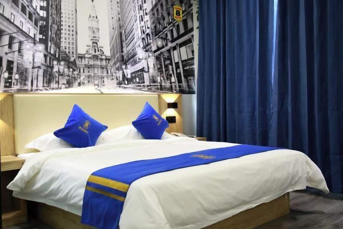 A hotel room with a bed, a headboard, a nightstand, a lamp, a curtain, and a wall mural.