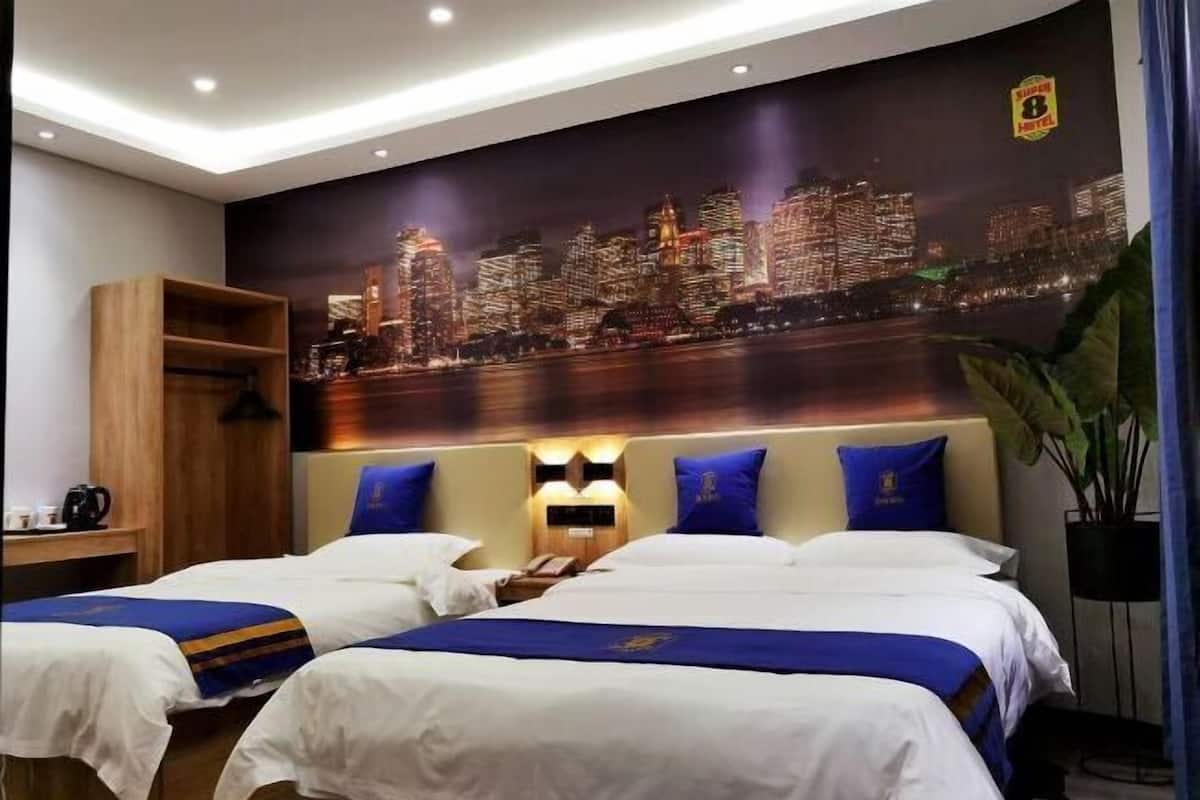 A hotel room with two beds, a cityscape mural, a wooden shelf, and a potted plant.