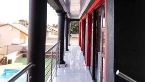 A covered outdoor corridor with a pool, black columns, and red-framed doors. - Milk and Honey Westonaria (Westonaria)