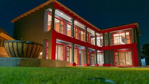 A modern two-story building with a red and grey facade, large windows, and a well-maintained lawn. - Milk and Honey Westonaria (Westonaria)