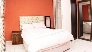 A bedroom with a bed, a nightstand, a wardrobe, and a mirror. - Milk and Honey Westonaria (Westonaria)