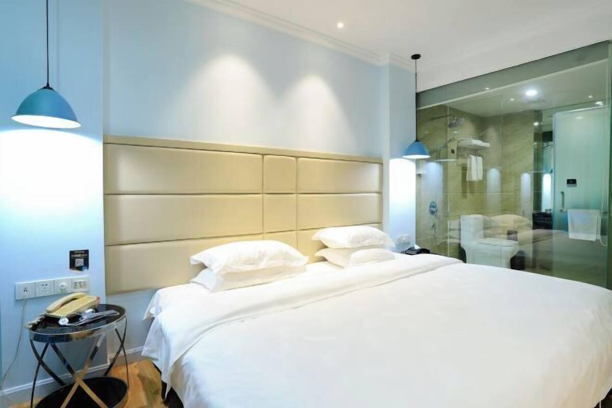 A hotel room with a bed, bedside table, and a glass-enclosed shower area.