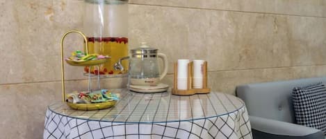 A table with a glass punch bowl, a coffee pot, and a tray with snacks.