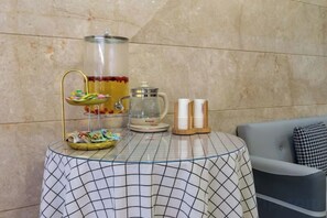 Uma mesa com uma compoteira de vidro, uma cafeteira e um suporte com petiscos.