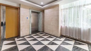 A hotel lobby with a checkered floor, a wooden door, a lift, and a window with sheer curtains. - Guangzhou Dipai Hotel (Nansha Jinzhou) (Guangzhou)