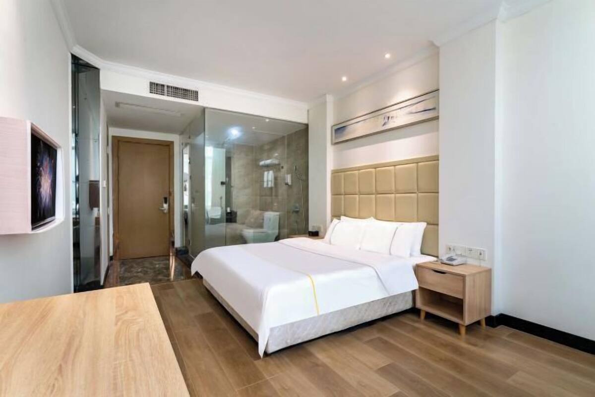 A hotel room with a bed, bedside table, and a glass partition wall.