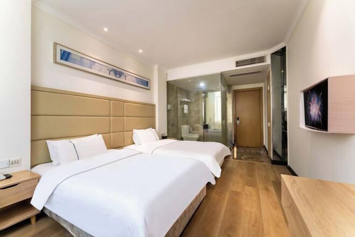 A hotel room with two beds, a wooden floor, a large artwork on the wall, and a television on the right.