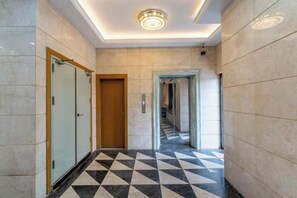 Un pasillo con piso de cuadros, una puerta de madera y una lámpara en el techo.