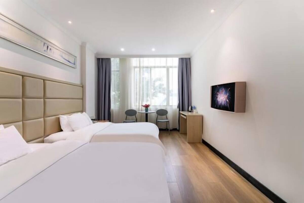 A hotel room with two beds, a desk, a chair, a small table, and a window with curtains.