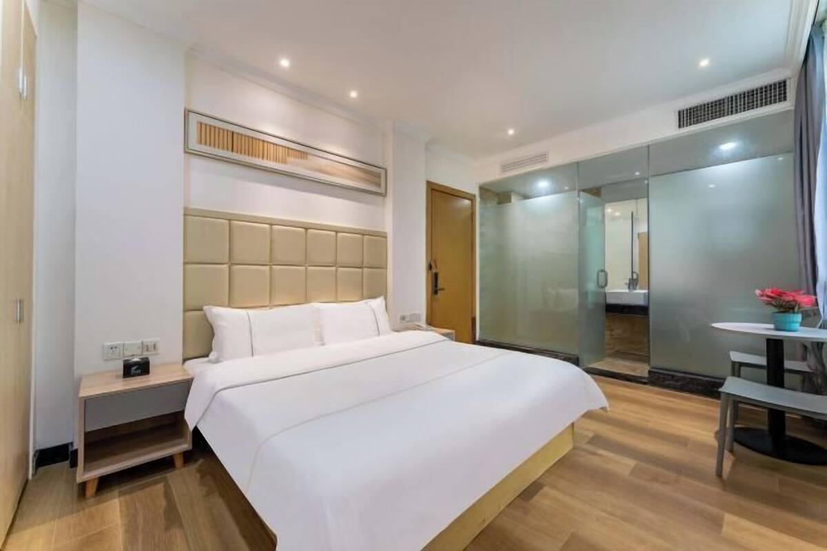 A modern hotel room with a large bed, a bedside table, a mirror, and a small table with a plant.