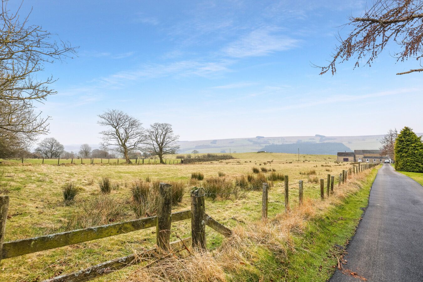 A rural landscape with a paved road, open fields, and a distant building.