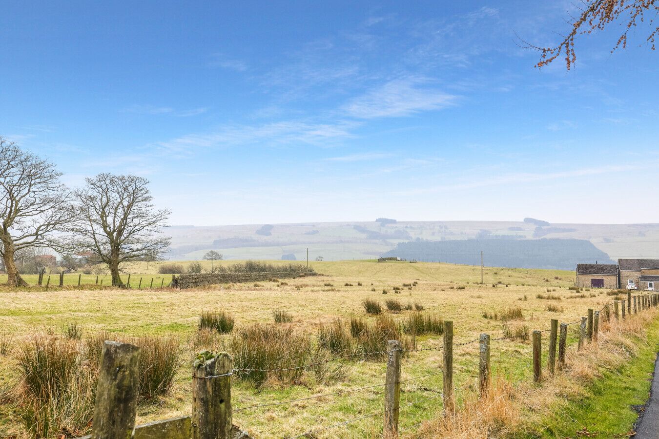 Un paysage rural avec un mur de pierres, une clôture en bois et un bâtiment visible au loin.