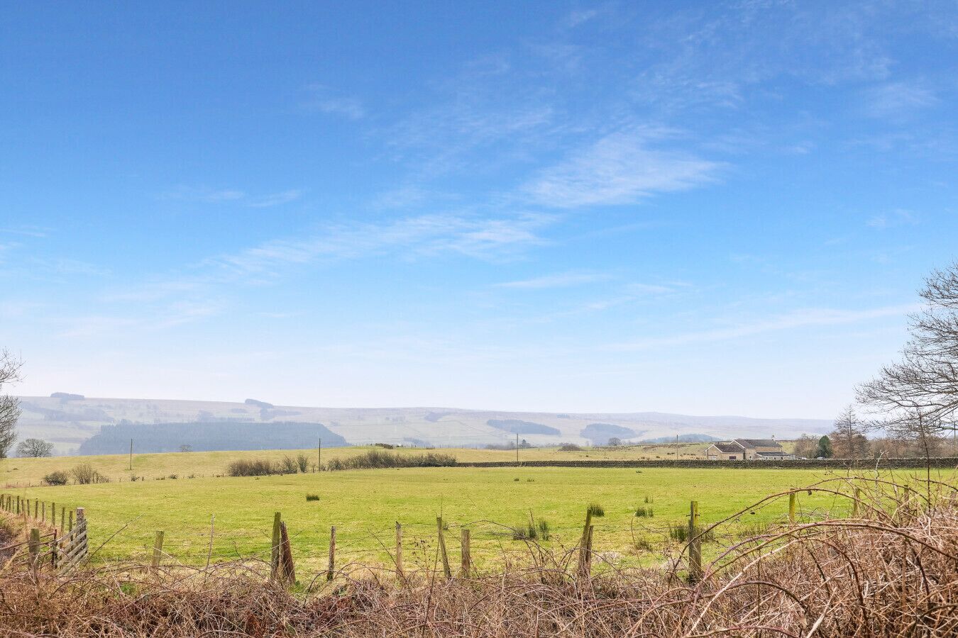 Un paysage rural avec de vastes champs, une clôture et des bâtiments situés au loin.
