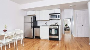 Una cocina compacta con armarios blancos, microondas, refrigerador, lavavajillas y estufa.