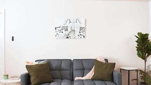 Una sala de estar moderna con un sofá gris, dos cojines verdes, una mesita redonda y una planta en maceta.