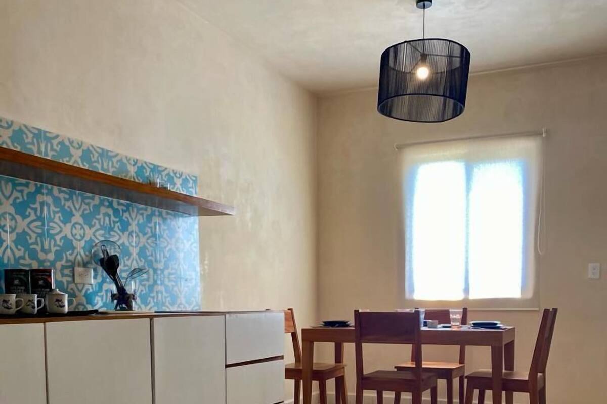 Cozinha com área de refeições, destacando um mosaico de backsplash, luminária pendente e janela com cortinas.