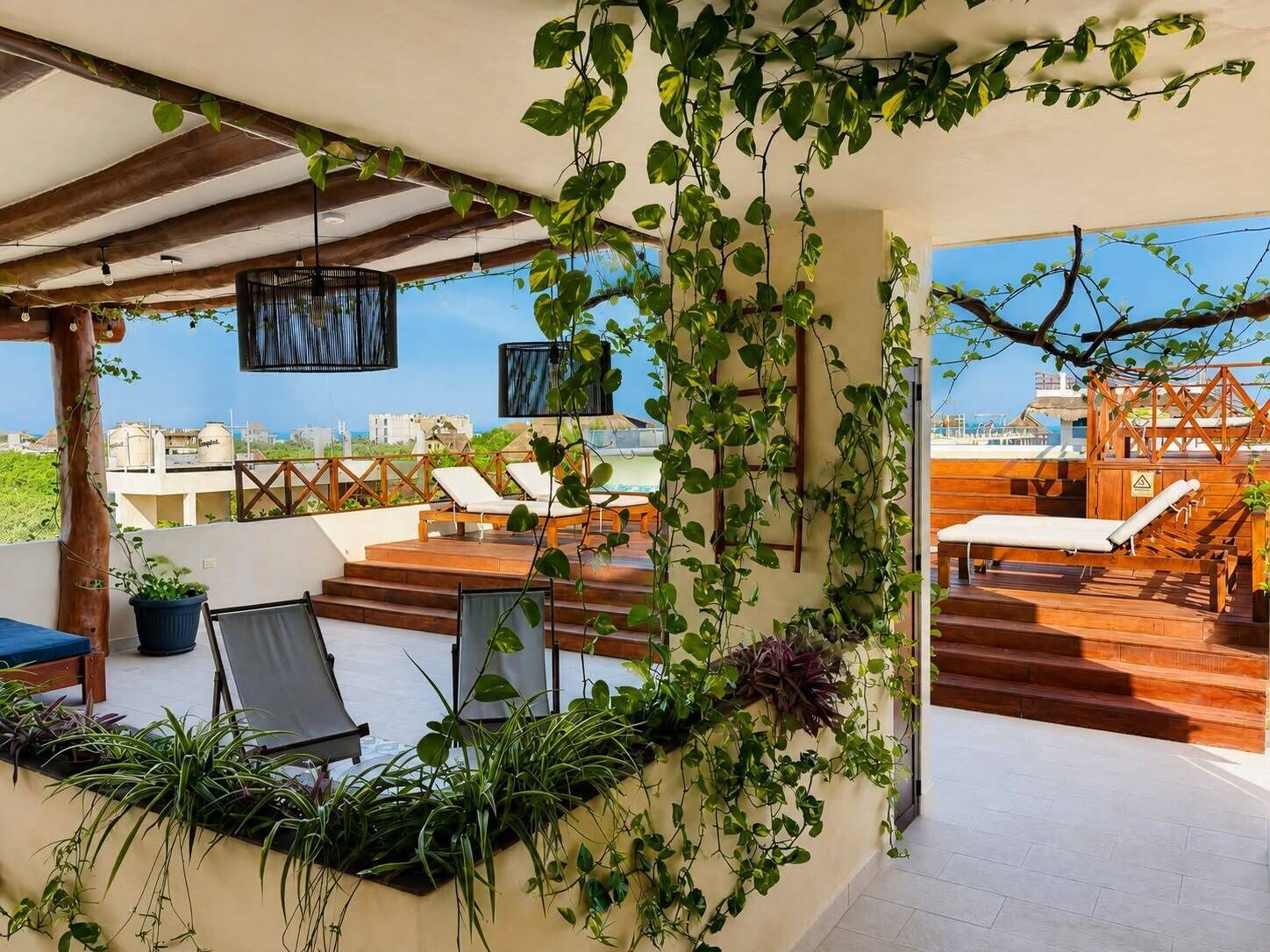 A rooftop terrace with lounge chairs, a wooden staircase, and lush greenery.