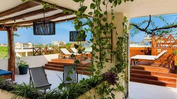 A rooftop terrace with lounge chairs, a wooden staircase, and lush greenery.