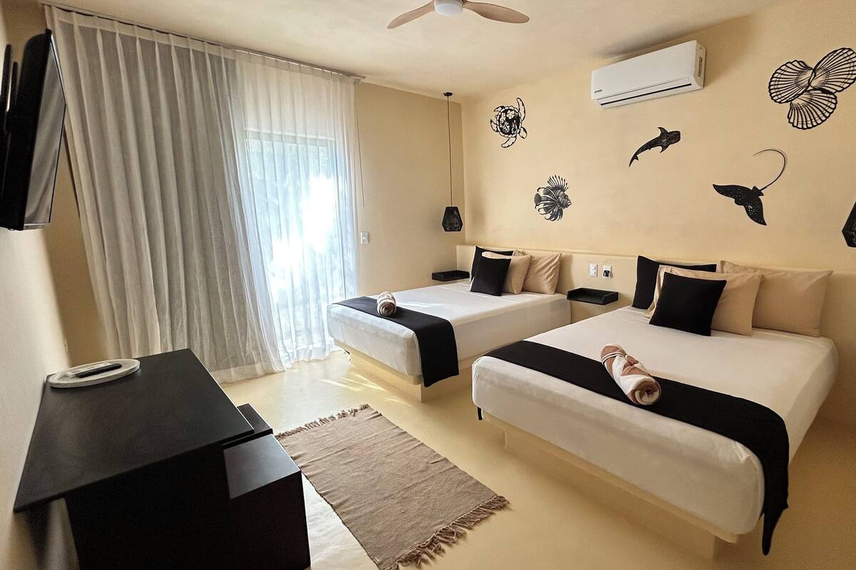 Quarto de hotel com duas camas, uma escrivaninha e uma janela grande com cortinas.